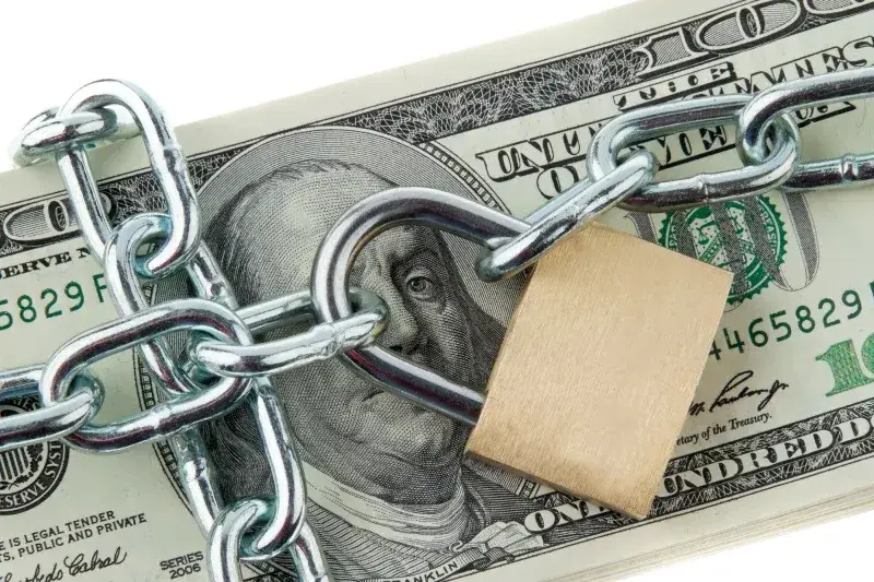 A stack of hundred dollar bills wrapped in a steel chain and padlock