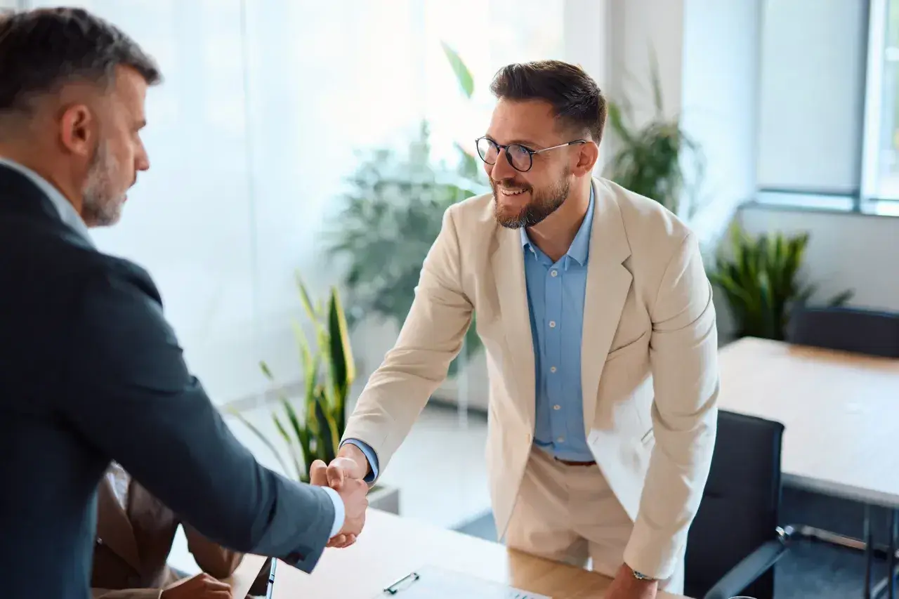 Two people shaking hands across a desk in a small office